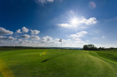 Parlak güneşli bir günde bir yeşil golf sahası, delik ve bayrak görünümünü. Spor, sakin ol, rekreasyon ve eğlence kavramı. Güneş ışınları, yaz yatay