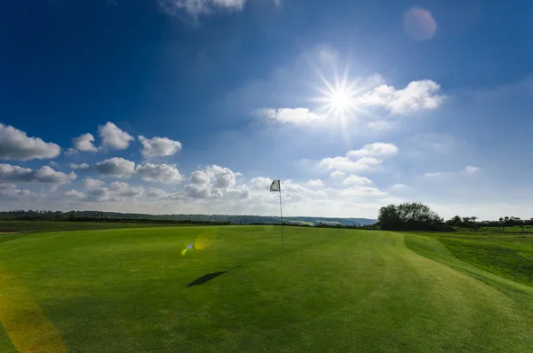 Utsikt över en grön golfbana, hål och flagga på en solig dag. Sport, relax, rekreation och fritid-konceptet. Sommarlandskap med solstrålar — Stockfoto