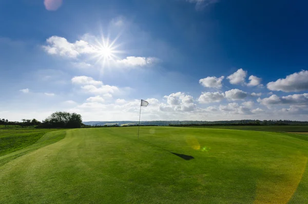 Vista de um campo de golfe verde, buraco e bandeira em um dia ensolarado brilhante. Desporto, relaxamento, recreação e lazer conceito. Paisagem de verão com raios de sol — Fotografia de Stock