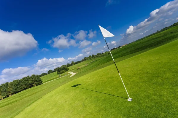 Utsikt över en grön golfbana, hål och flagga på en solig dag. Sport, relax, rekreation och fritid-konceptet. Sommarlandskap med solstrålar — Stockfoto