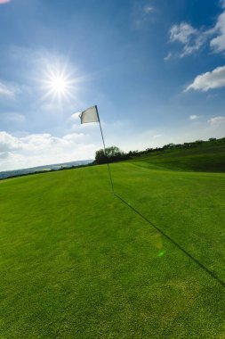 Parlak güneşli bir günde bir yeşil golf sahası, delik ve bayrak görünümünü. Spor, sakin ol, rekreasyon ve eğlence kavramı. Güneş ışınları, yaz yatay