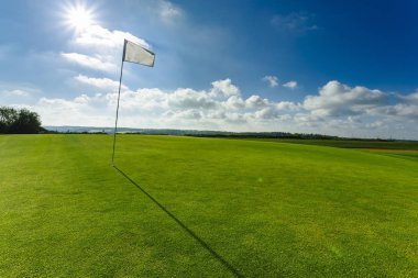 Parlak güneşli bir günde bir yeşil golf sahası, delik ve bayrak görünümünü. Spor, sakin ol, rekreasyon ve eğlence kavramı. Güneş ışınları, yaz yatay