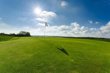 Parlak güneşli bir günde bir yeşil golf sahası, delik ve bayrak görünümünü. Spor, sakin ol, rekreasyon ve eğlence kavramı. Güneş ışınları, yaz yatay