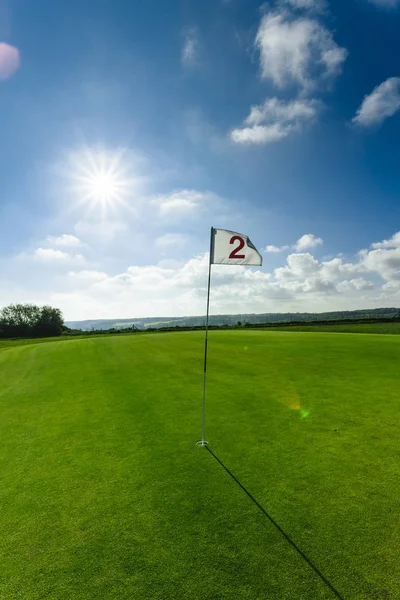 Вид на зеленое поле для гольфа, лунку и флаг в яркий солнечный день. Спорт, отдых, отдых и досуг концепция. Летний пейзаж с солнечными лучами — стоковое фото