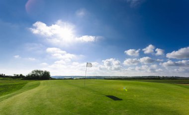 Parlak güneşli bir günde bir yeşil golf sahası, delik ve bayrak görünümünü. Spor, sakin ol, rekreasyon ve eğlence kavramı. Güneş ışınları, yaz yatay