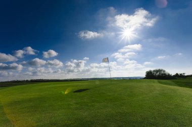 Parlak güneşli bir günde bir yeşil golf sahası, delik ve bayrak görünümünü. Spor, sakin ol, rekreasyon ve eğlence kavramı. Güneş ışınları, yaz yatay