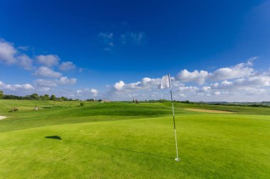 Parlak güneşli bir günde bir yeşil golf sahası, delik ve bayrak görünümünü. Spor, sakin ol, rekreasyon ve eğlence kavramı. Güneş ışınları, yaz yatay