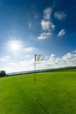 Parlak güneşli bir günde bir yeşil golf sahası, delik ve bayrak görünümünü. Spor, sakin ol, rekreasyon ve eğlence kavramı. Güneş ışınları, yaz yatay