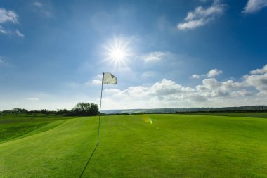 Parlak güneşli bir günde bir yeşil golf sahası, delik ve bayrak görünümünü. Spor, sakin ol, rekreasyon ve eğlence kavramı. Güneş ışınları, yaz yatay