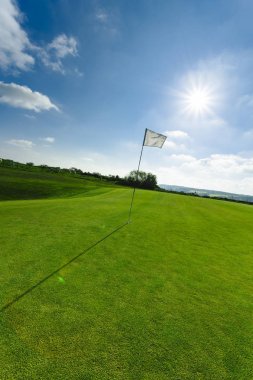 Parlak güneşli bir günde bir yeşil golf sahası, delik ve bayrak görünümünü. Spor, sakin ol, rekreasyon ve eğlence kavramı. Güneş ışınları, yaz yatay