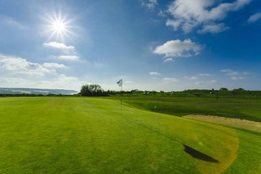 Parlak güneşli bir günde bir yeşil golf sahası, delik ve bayrak görünümünü. Spor, sakin ol, rekreasyon ve eğlence kavramı. Güneş ışınları, yaz yatay
