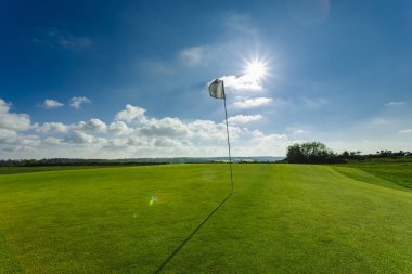 Parlak güneşli bir günde bir yeşil golf sahası, delik ve bayrak görünümünü. Spor, sakin ol, rekreasyon ve eğlence kavramı. Güneş ışınları, yaz yatay