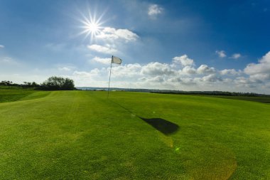 Parlak güneşli bir günde bir yeşil golf sahası, delik ve bayrak görünümünü. Spor, sakin ol, rekreasyon ve eğlence kavramı. Güneş ışınları, yaz yatay