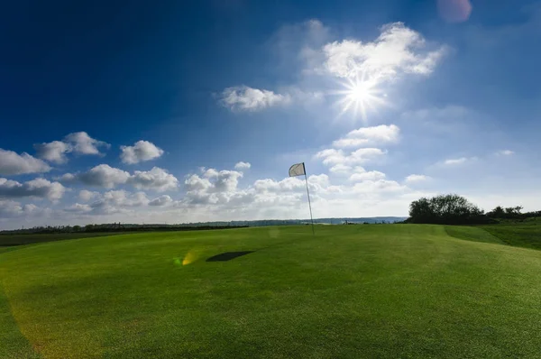 View of a green golf course, hole and flag on a bright sunny day. Sport, relax, recreation and leisure concept. Summer landscape with sunbeams — Stock Photo, Image