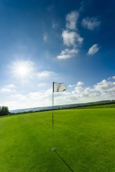 View of a green golf course, hole and flag on a bright sunny day. Sport, relax, recreation and leisure concept. Summer landscape with sunbeams — Stock Photo, Image
