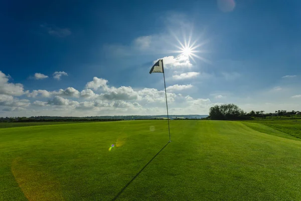 View of a green golf course, hole and flag on a bright sunny day. Sport, relax, recreation and leisure concept. Summer landscape with sunbeams