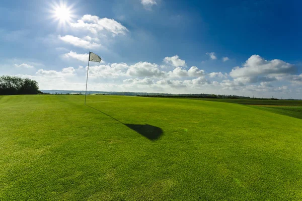 Vista de um campo de golfe verde, buraco e bandeira em um dia ensolarado brilhante. Desporto, relaxamento, recreação e lazer conceito. Paisagem de verão com raios de sol — Fotografia de Stock
