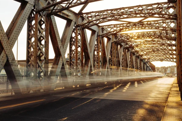 Asphalt road under the steel construction of a city bridge on a sunny day. Urban scene in the bridge tunnel. Long exposure. Toned — Stock Photo, Image