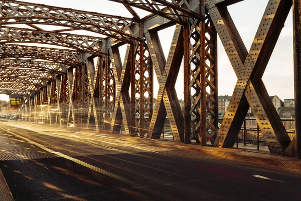 Camino de asfalto bajo la construcción de acero de un puente de la ciudad en un día soleado. Escena urbana en el túnel del puente. Larga exposición. Tonificado —  Fotos de Stock