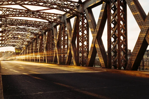 Asphalt road under the steel construction of a city bridge on a sunny day. Urban scene in the bridge tunnel. Long exposure. Toned — Stock Photo, Image