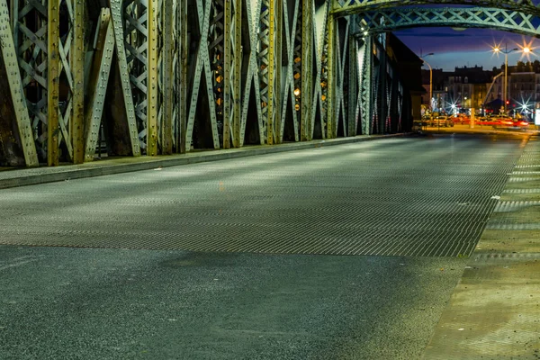 Camino de asfalto bajo la construcción de acero de un puente en la ciudad. Escena urbana nocturna con senderos de luz de coche en el túnel. Tonificado — Foto de Stock