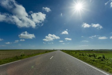Yeşil ve çiçekli tarım alanları geçerken boş asfalt köy yolunda. Fransa'da bir güneşli bahar gününde kırsal manzara. Çevre dostu tarım, sanayi tarım kavramı