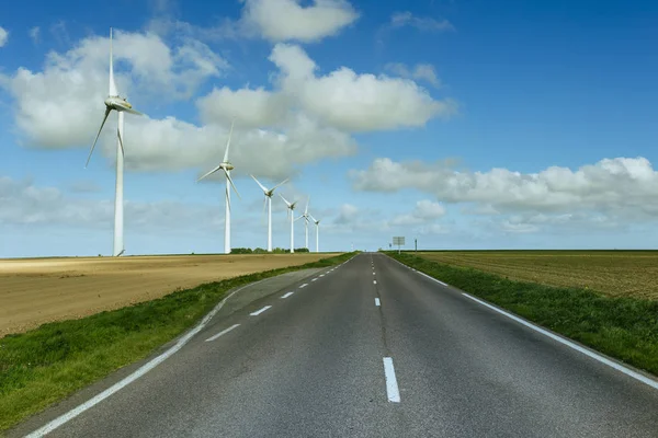 Estrada rural asfalto vazio passando por campos agrícolas verdes e floridos. Paisagem no campo em um dia ensolarado de primavera na França. Agricultura amiga do ambiente, conceito de agricultura industrial — Fotografia de Stock