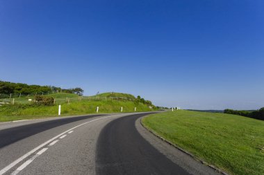 Yeşil alanları üzerinden geçen virajlı yol boş asfalt. Normandy, Fransa için kırsal manzara parlak güneşli bir günde. Taşıma, endüstriyel tarım, tatil ve yol ağ kavramı