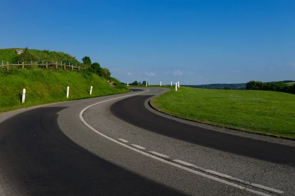 Empty asphalt curvy road passing through green fields. Countryside landscape on a bright sunny day in Normandy, France. Transport, industrial agriculture, holiday and road network concept — Stock Photo, Image