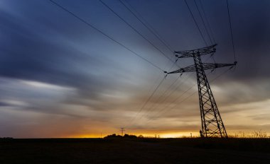 Yüksek gerilim enerji hatları ve enerji nakil direkleri gün batımında. Pole ve çizgiler siluetleri dusk içinde. Elektrik üretim ve dağıtım. Elektrik Sanayi ve doğa genel kavram. Uzun pozlama