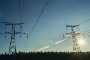 Yüksek gerilim enerji hatları ve enerji nakil direkleri Normandy, Fransa için mavi gökyüzünde güneş ışınları ile. Kırsal manzara. Elektrik üretim ve dağıtım. Elektrik Sanayi ve doğa