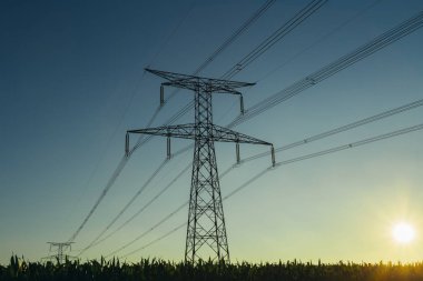 Yüksek gerilim enerji hatları ve enerji nakil direkleri Normandy, Fransa için mavi gökyüzünde güneş ışınları ile. Kırsal manzara. Elektrik üretim ve dağıtım. Elektrik Sanayi ve doğa