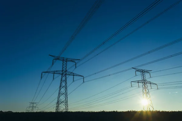 Yüksek gerilim enerji hatları ve enerji nakil direkleri Normandy, Fransa için mavi gökyüzünde güneş ışınları ile. Kırsal manzara. Elektrik üretim ve dağıtım. Elektrik Sanayi ve doğa