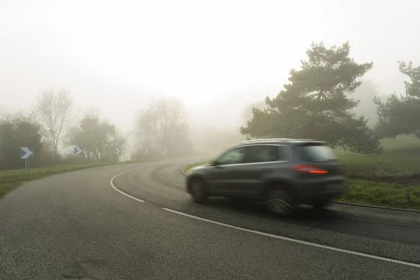 Ομιχλώδης ασφαλτοστρωμένο δρόμο καμπύλη με αυτοκίνητα που διέρχονται μέσα από το δάσος. Καιρικές συνθήκες με περιορισμένη ορατότητα στην περιοχή του Νορμανδία, Γαλλία. Χώρα τοπίο ομιχλώδη ημέρα. Ήπια — Φωτογραφία Αρχείου