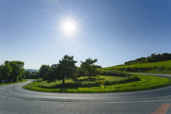 Prázdné asfaltové vlnité silnice procházející zelené louky a lesy. Venkovské krajiny na slunný jarní den ve Francii. Sluneční paprsky na obloze. Doprava, průmyslové zemědělství, koncepce silniční sítě — Stock fotografie