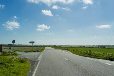 Yeşil ve çiçekli tarım alanları geçerken boş asfalt köy yolunda. Fransa'da bir güneşli bahar gününde kırsal manzara. Çevre dostu tarım, sanayi tarım kavramı