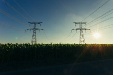 Yüksek gerilim enerji hatları ve enerji nakil direkleri Normandy, Fransa için mavi gökyüzünde güneş ışınları ile. Kırsal manzara. Elektrik üretim ve dağıtım. Elektrik Sanayi ve doğa