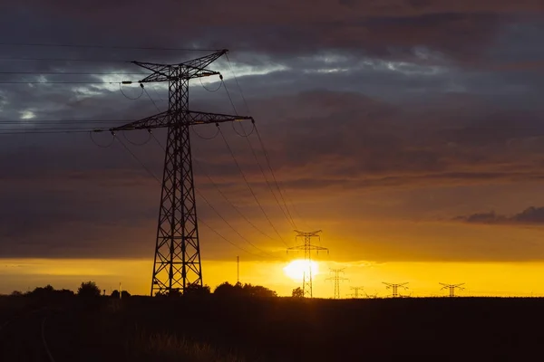 Linie wysokiego napięcia i wież transmisyjnych o zachodzie słońca. Polacy i napowietrznych linii sylwetki w zmierzchu. Wytwarzanie energii elektrycznej i dystrybucji. Koncepcja przemysłu i charakter energii elektrycznej — Zdjęcie stockowe