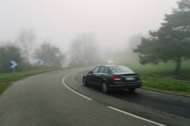 Ormanın içinden geçen arabalar ile eğri yol sisli asfalt. Normandy, Fransa bölgedeki düşük görünürlük ile hava durumu. Ülke manzara sisli gün. Tonda