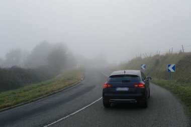 Ormanın içinden geçen arabalar ile eğri yol sisli asfalt. Normandy, Fransa bölgedeki düşük görünürlük ile hava durumu. Ülke manzara sisli gün. Tonda