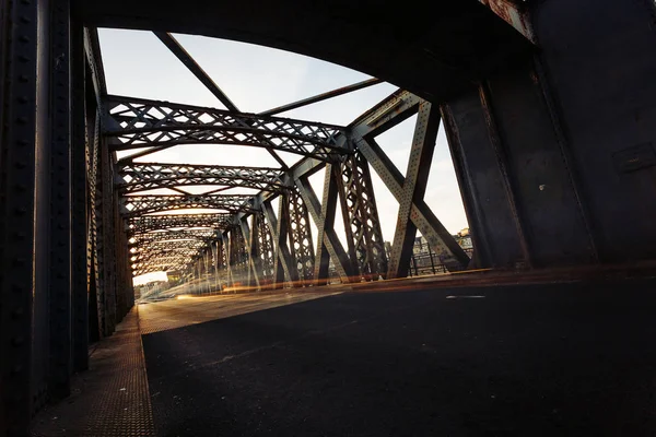 Estrada de asfalto sob a construção de aço de uma ponte da cidade em um dia ensolarado. Cena urbana no túnel da ponte. Longa exposição. Tonificado — Fotografia de Stock