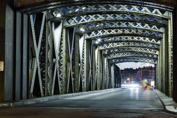 Asphalt road under the steel construction of a bridge in the city. Night urban scene with car light trails in the tunnel. Toned — Stock Photo, Image