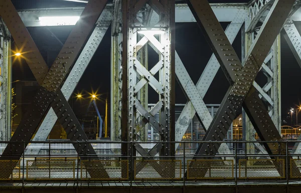 Asphalt road under the steel construction of a bridge in the city. Night urban scene with car light trails in the tunnel. Toned — Stock Photo, Image