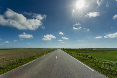 Yeşil ve çiçekli tarım alanları geçerken boş asfalt köy yolunda. Fransa'da bir güneşli bahar gününde kırsal manzara. Çevre dostu tarım, sanayi tarım kavramı