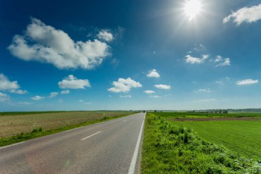 Yeşil ve çiçekli tarım alanları geçerken boş asfalt köy yolunda. Fransa'da bir güneşli bahar gününde kırsal manzara. Çevre dostu tarım, sanayi tarım kavramı
