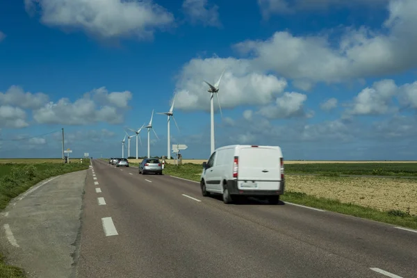 Carros que passam na estrada rural de asfalto através de campos agrícolas verdes e floridos. Paisagem do campo em um dia ensolarado na França. Agricultura amiga do ambiente, conceito de agricultura industrial — Fotografia de Stock