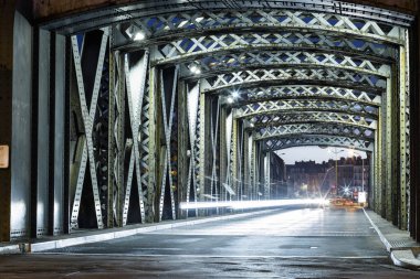 Asphalt road under the steel construction of a bridge in the city. Night urban scene with car light trails in the tunnel. Toned clipart