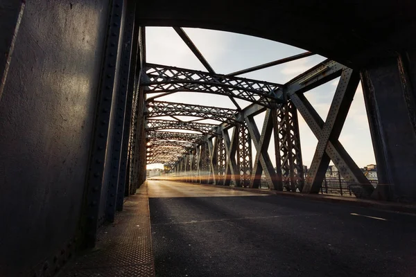 Ασφαλτοστρωμένος δρόμος κάτω από την κατασκευή του χάλυβα από μια γέφυρα της πόλης σε μια ηλιόλουστη ημέρα. Αστικό τοπίο στη σήραγγα γέφυρα. Μακροχρόνια έκθεση. Ήπια — Φωτογραφία Αρχείου