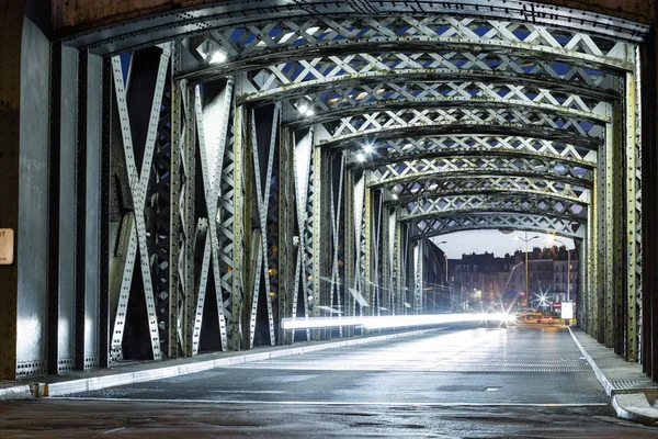 Asphalt road under the steel construction of a bridge in the city. Night urban scene with car light trails in the tunnel. Toned — Stock Photo, Image