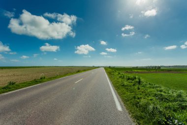Normandy, Fransa güneşli bir günde yeşil tarım alanları üzerinden geçen ülke yol boş asfalt. Kırsal manzara mavi gökyüzünde güneş ışınları ile yol ağ ve ulaşım konsepti